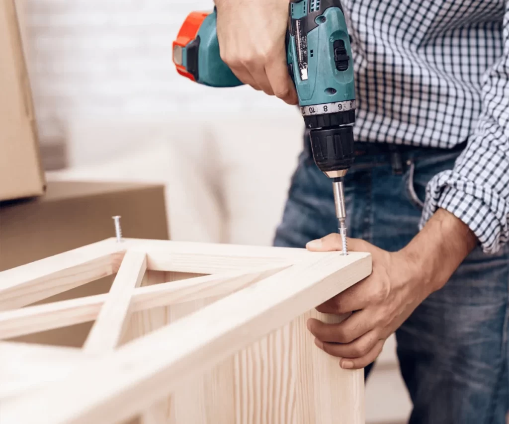 Carpenter assembling wooden furniture with a power drill in Dubai